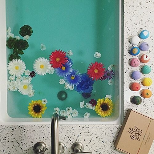 A bathtub filled with water, flowers, and bath bombs on the side.