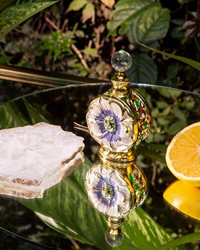 Decorative perfume bottle with floral design on a mirror with orange slice and mineral.