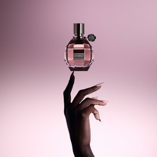 Hand balancing a perfume bottle on finger against pink background.