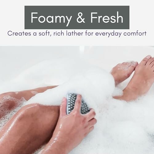 Person in a bathtub using a soapy sponge on their legs.