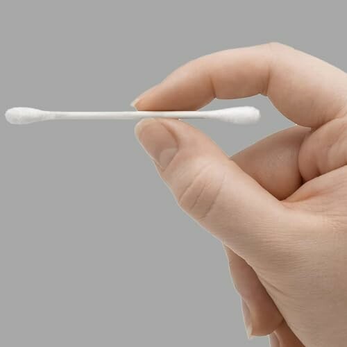 Hand holding a cotton swab against a gray background