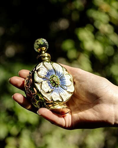 Hand holding a decorative perfume bottle with floral design.