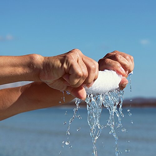 Hands squeezing water from a sponge outdoors.