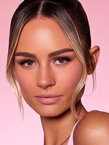 Close-up of a woman with makeup against a pink background.